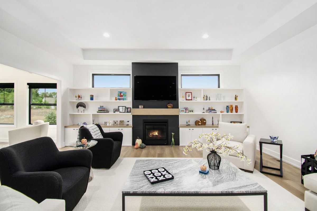 Modern living room with black chairs, a marble coffee table, and a fireplace. Built-in shelves display decor items, and large windows offer natural light.